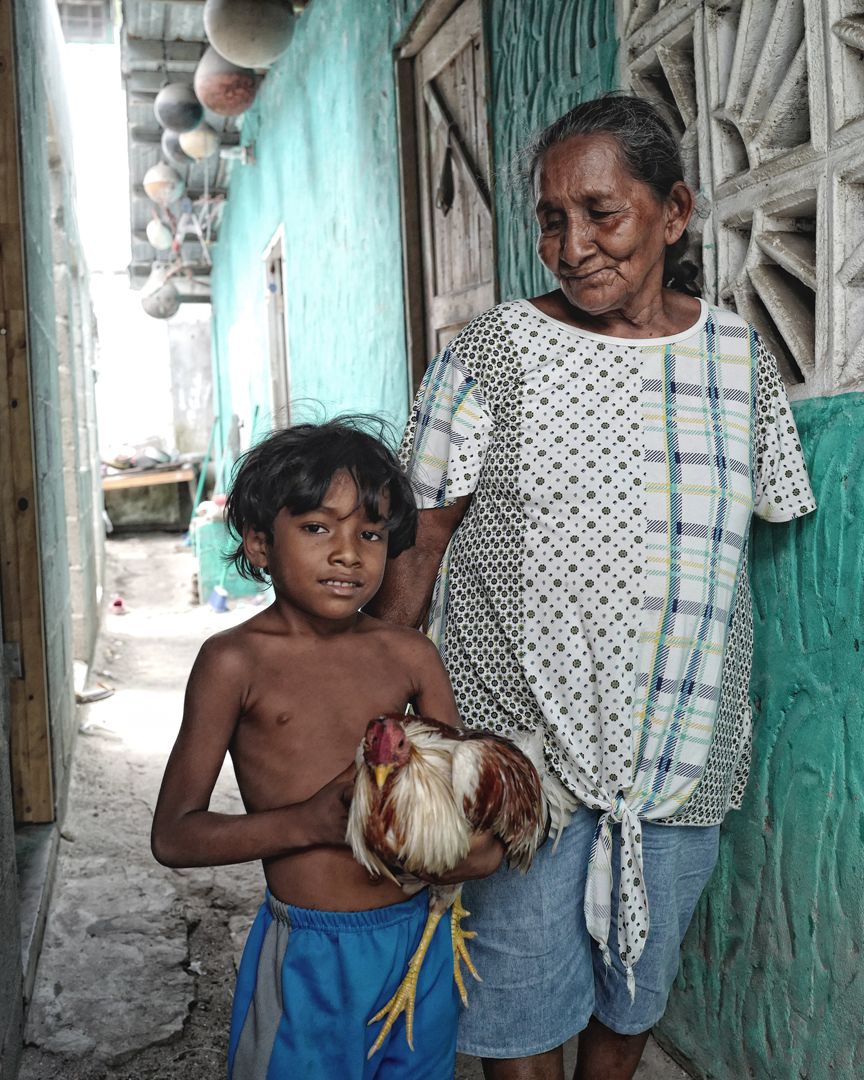 An elderly woman is standing in front of a fence.