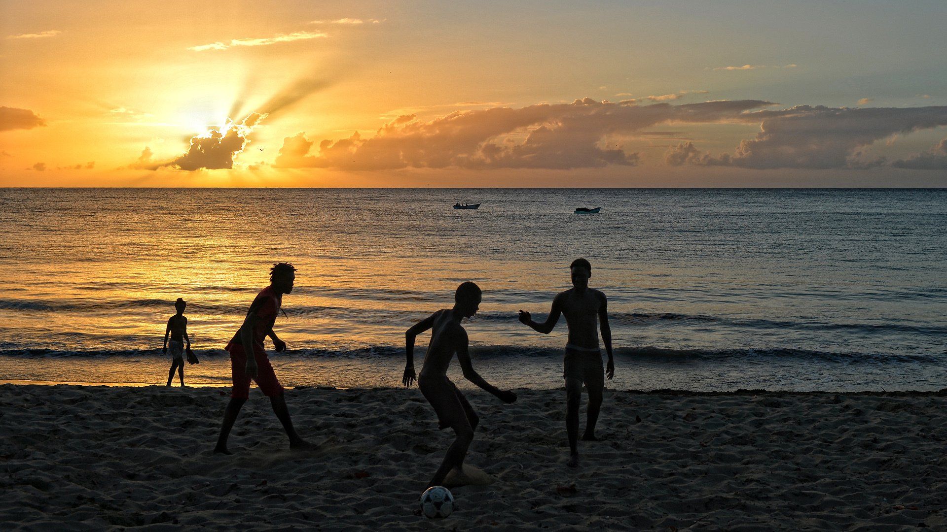 A group of people are playing soccer on the beach at sunset.