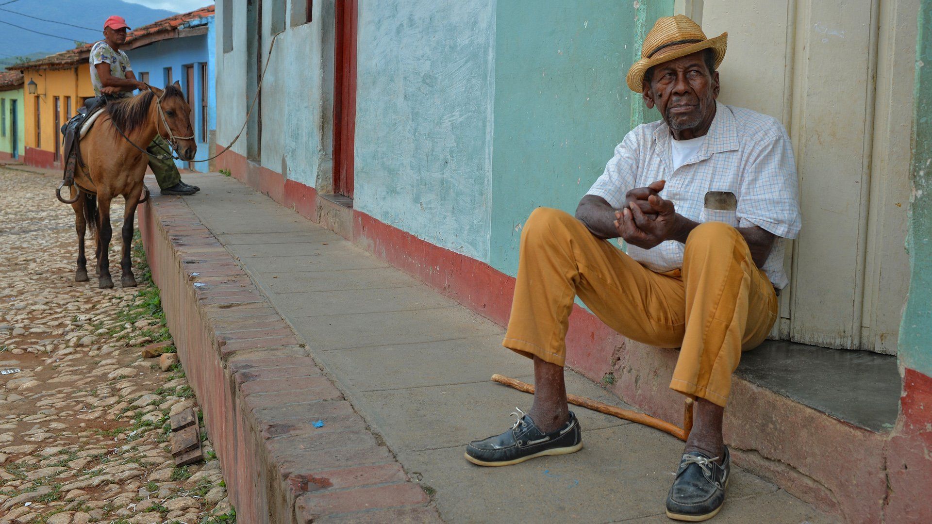 A man is sitting on the sidewalk next to a horse.