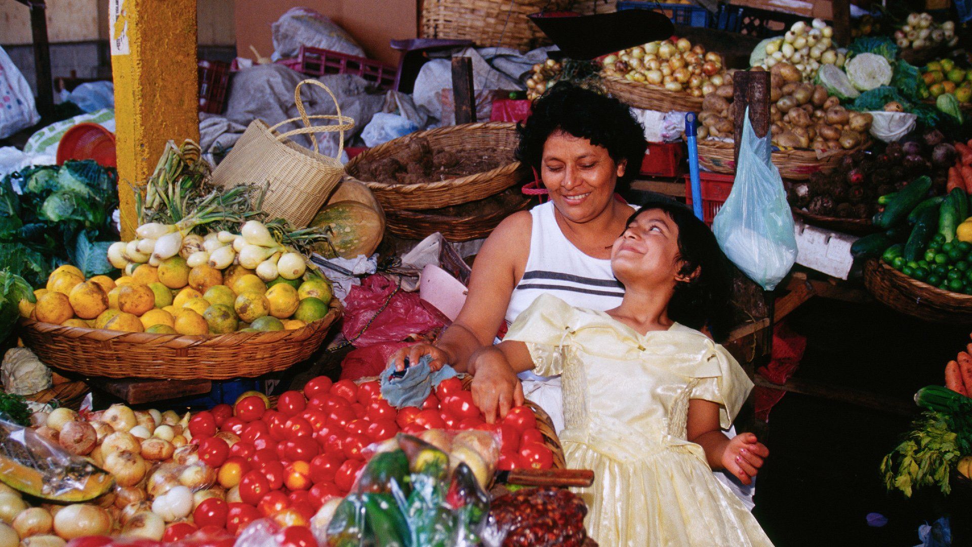 A woman and child are sitting in front of a fruit stand
