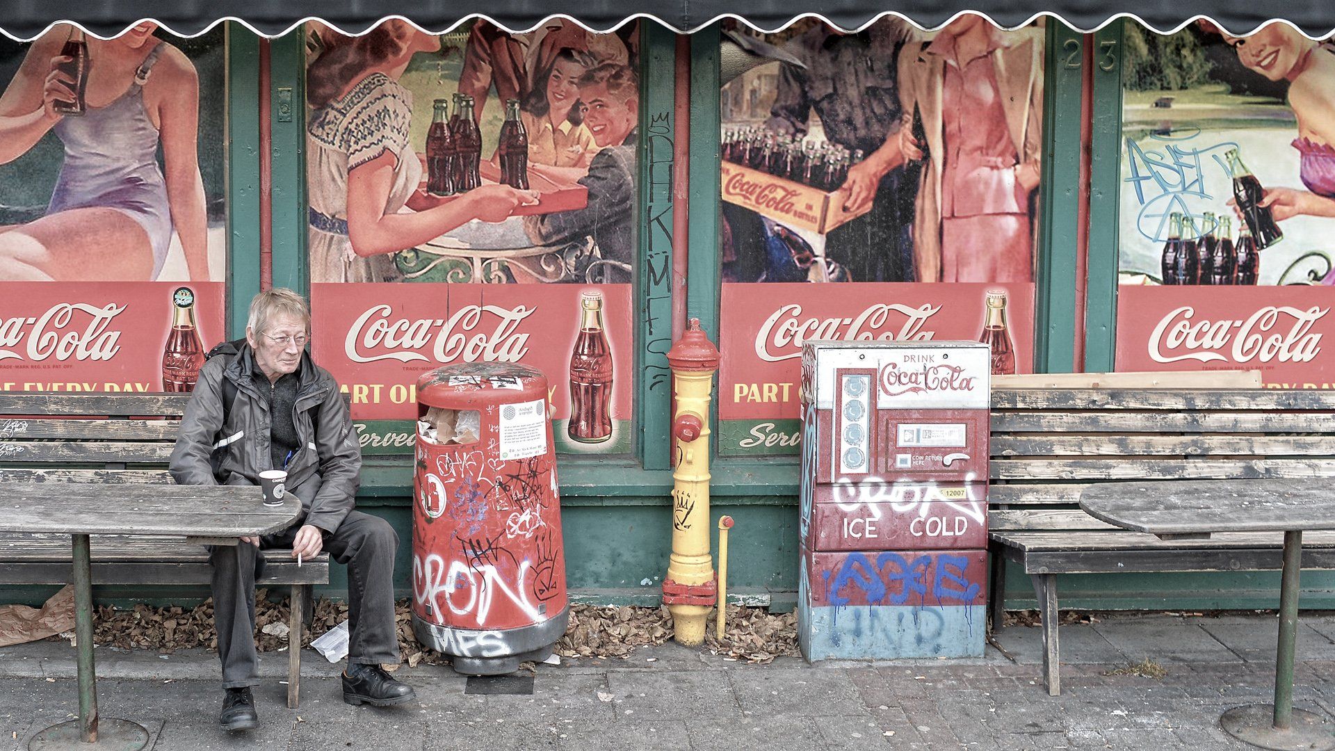 A man sits on a bench in front of a coca cola sign
