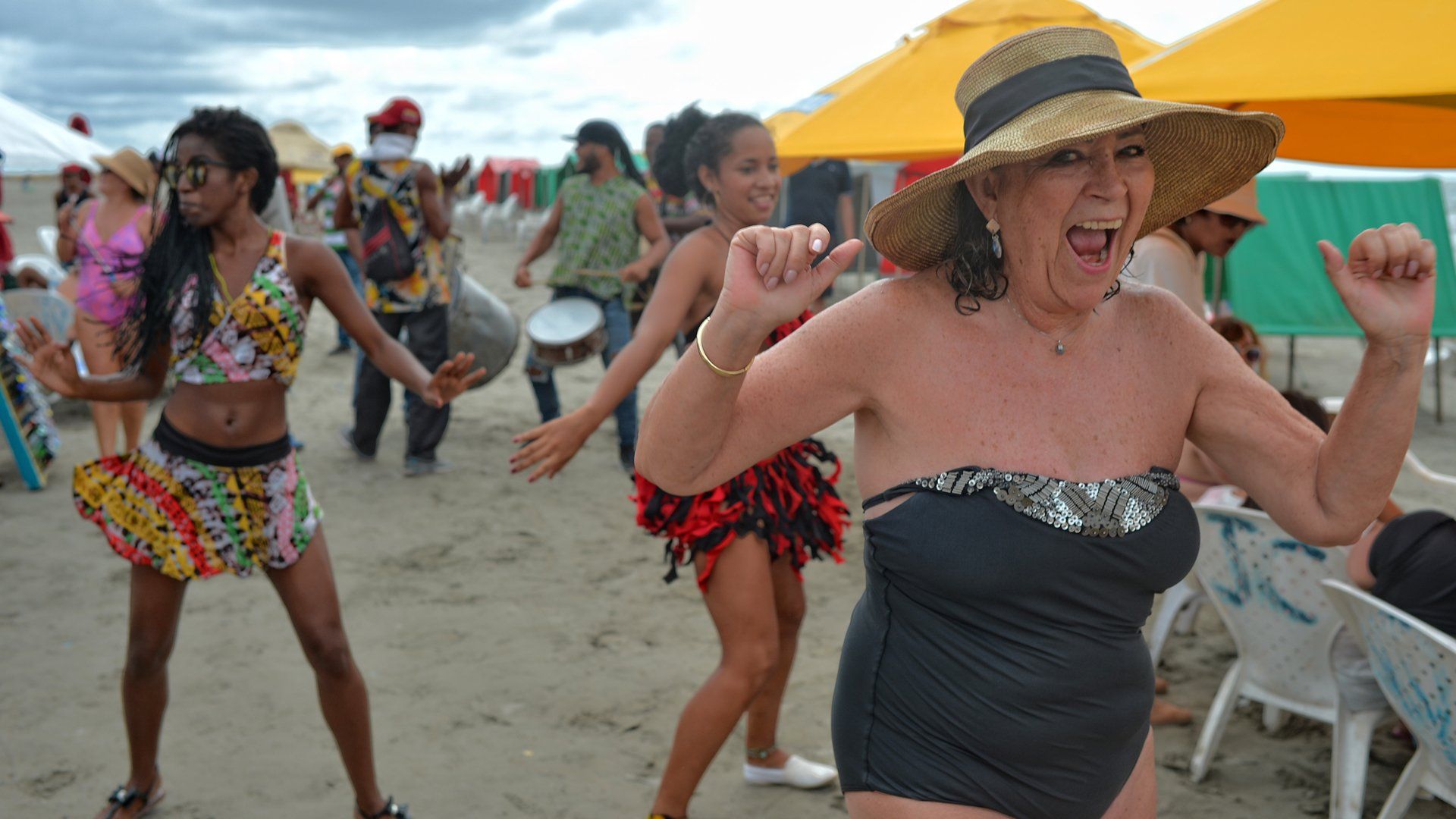 A woman in a bathing suit and hat is dancing on the beach.