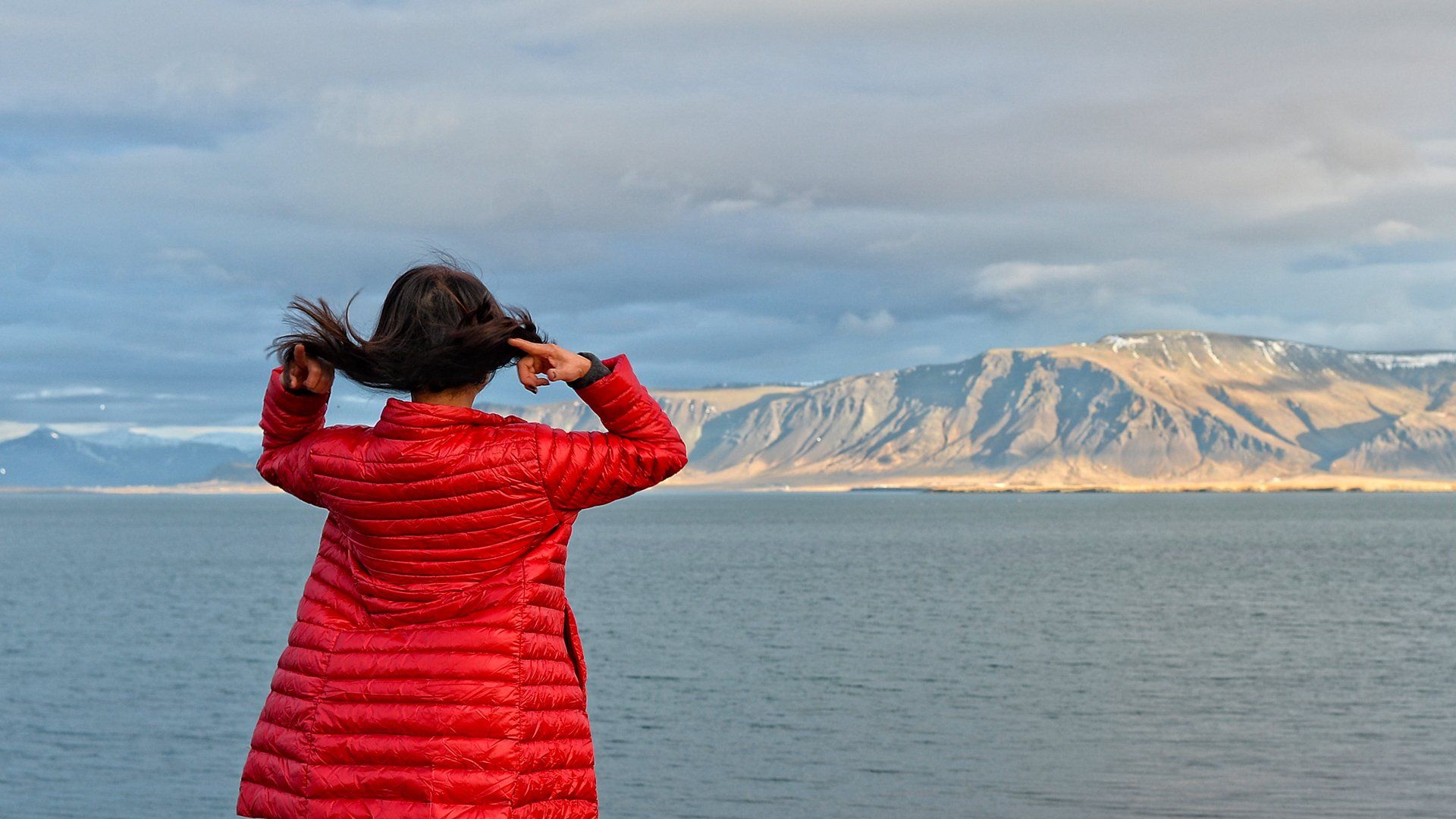 A woman in a red jacket is standing in front of a body of water.