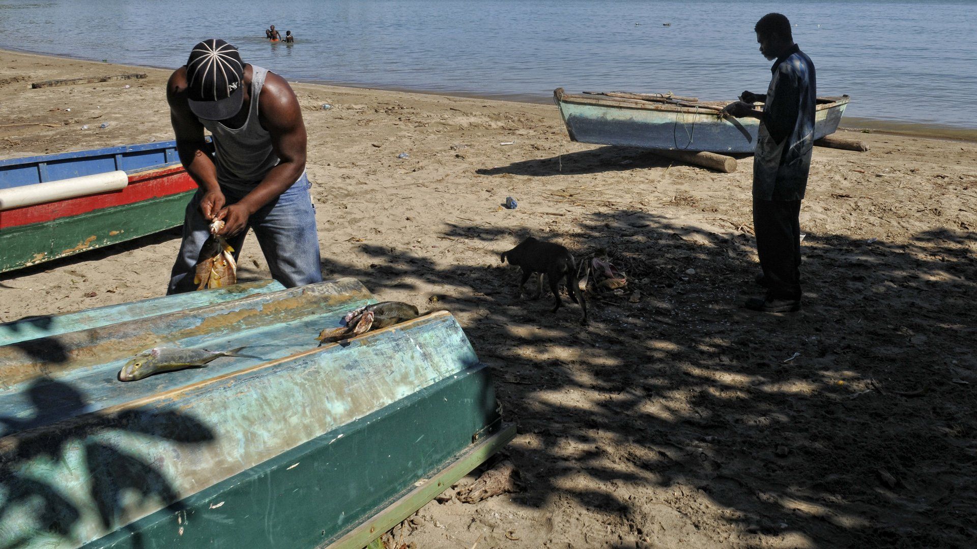 Two men are working on boats on the beach near the water.