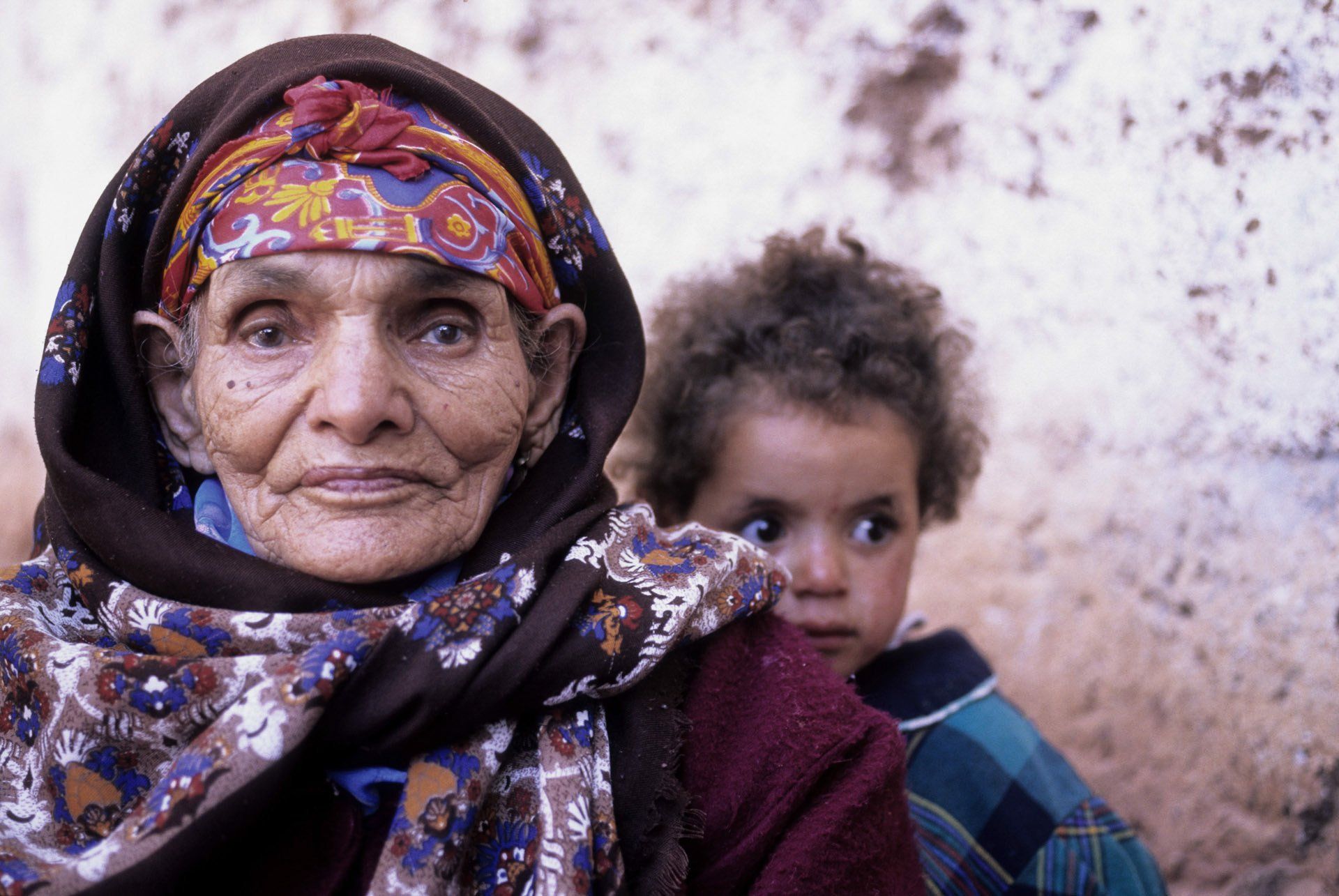 A woman with a scarf around her head is carrying a child on her back.