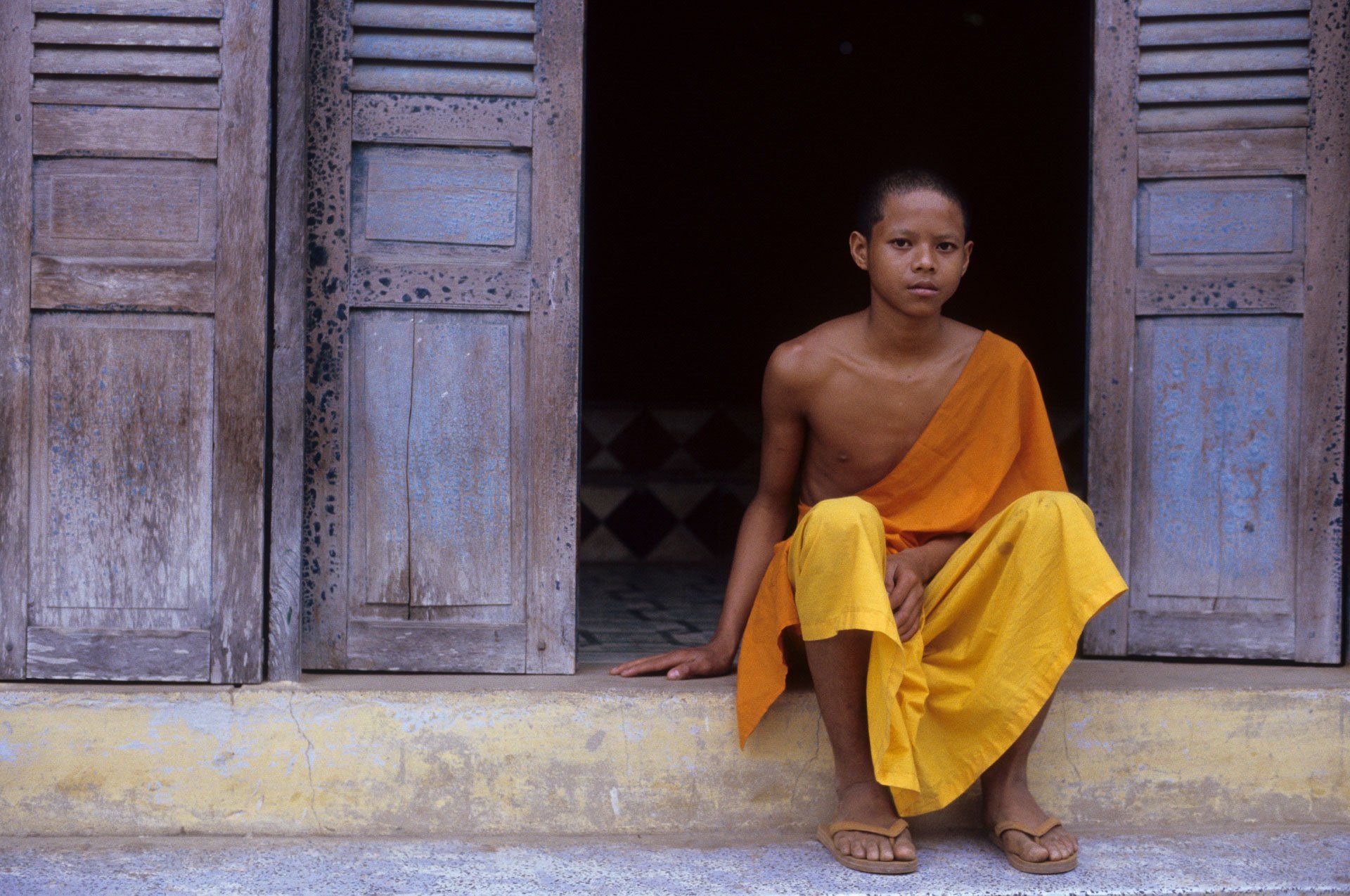 A young boy in a yellow robe is sitting on a doorstep