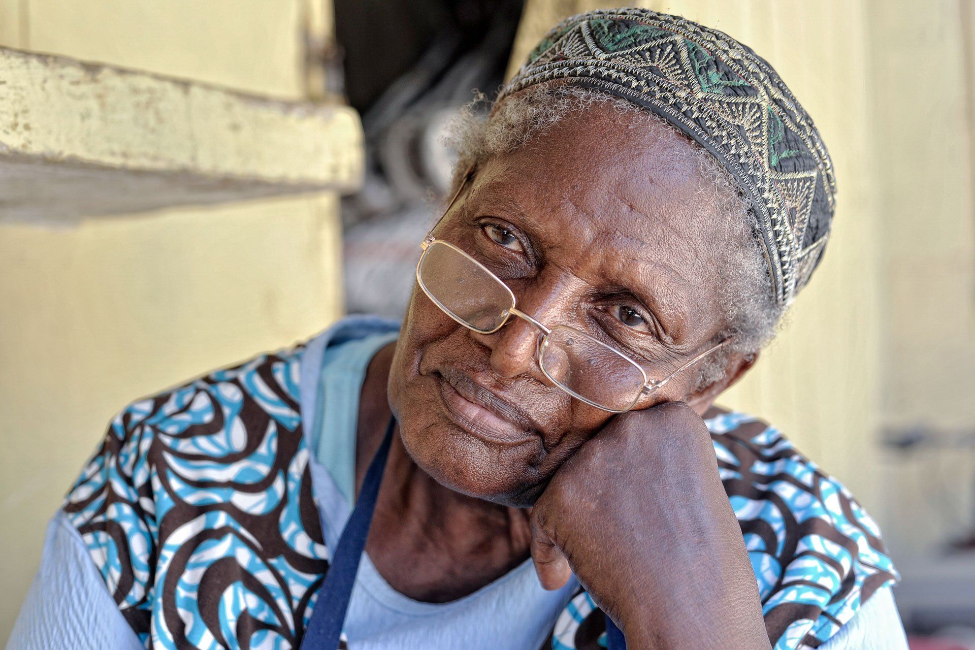 An elderly woman wearing glasses and a hat is smiling for the camera.