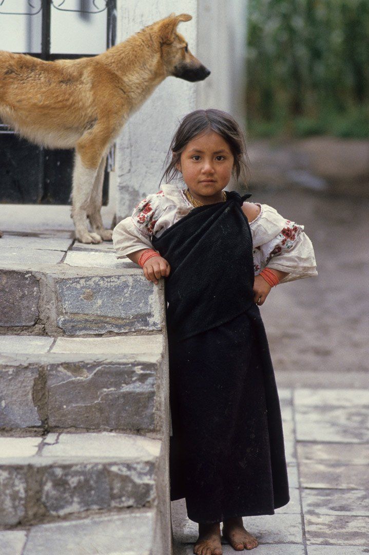 A little girl is standing next to a dog on a set of stairs.