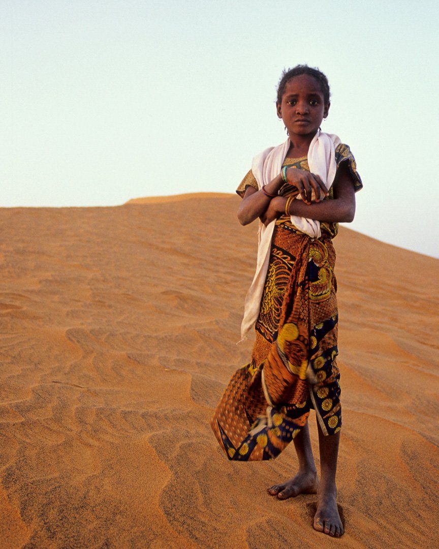 A young girl is standing in the middle of a desert with her arms crossed