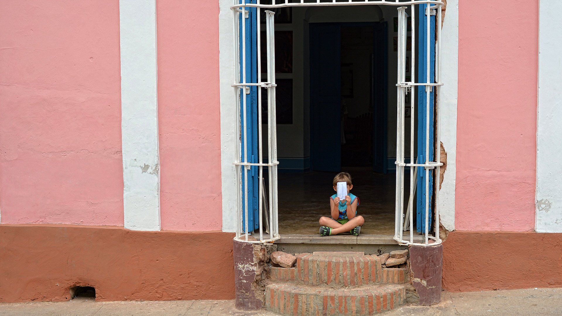 A child is sitting in the doorway of a pink and white building.