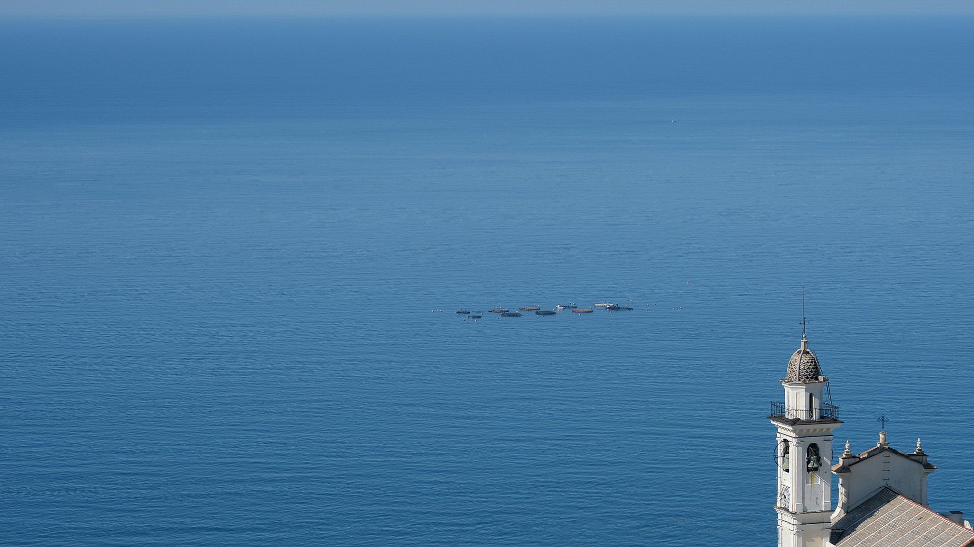 A church tower overlooking the ocean with dolphins swimming in the distance.