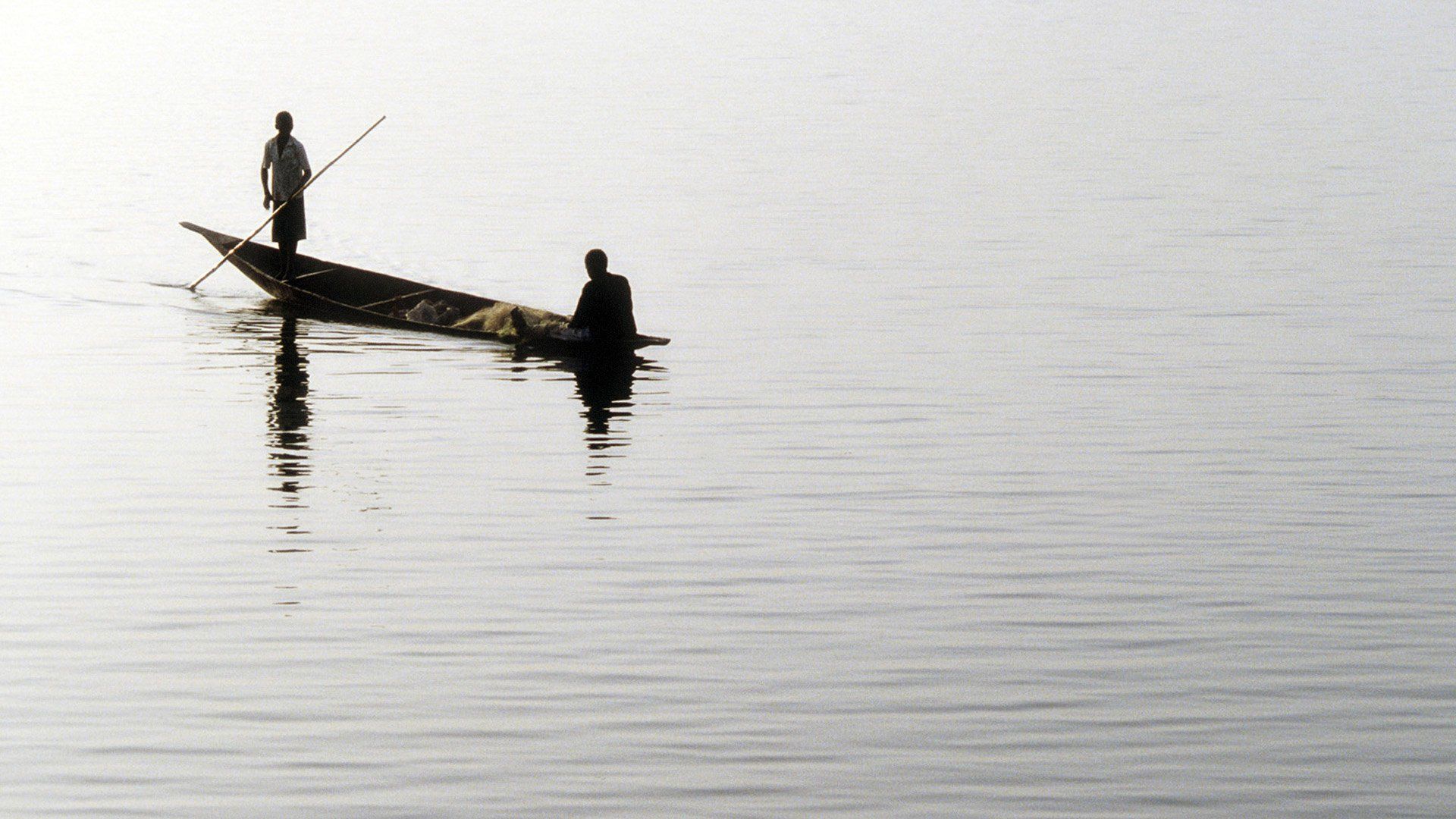 Two men are in a small boat in the middle of a lake.
