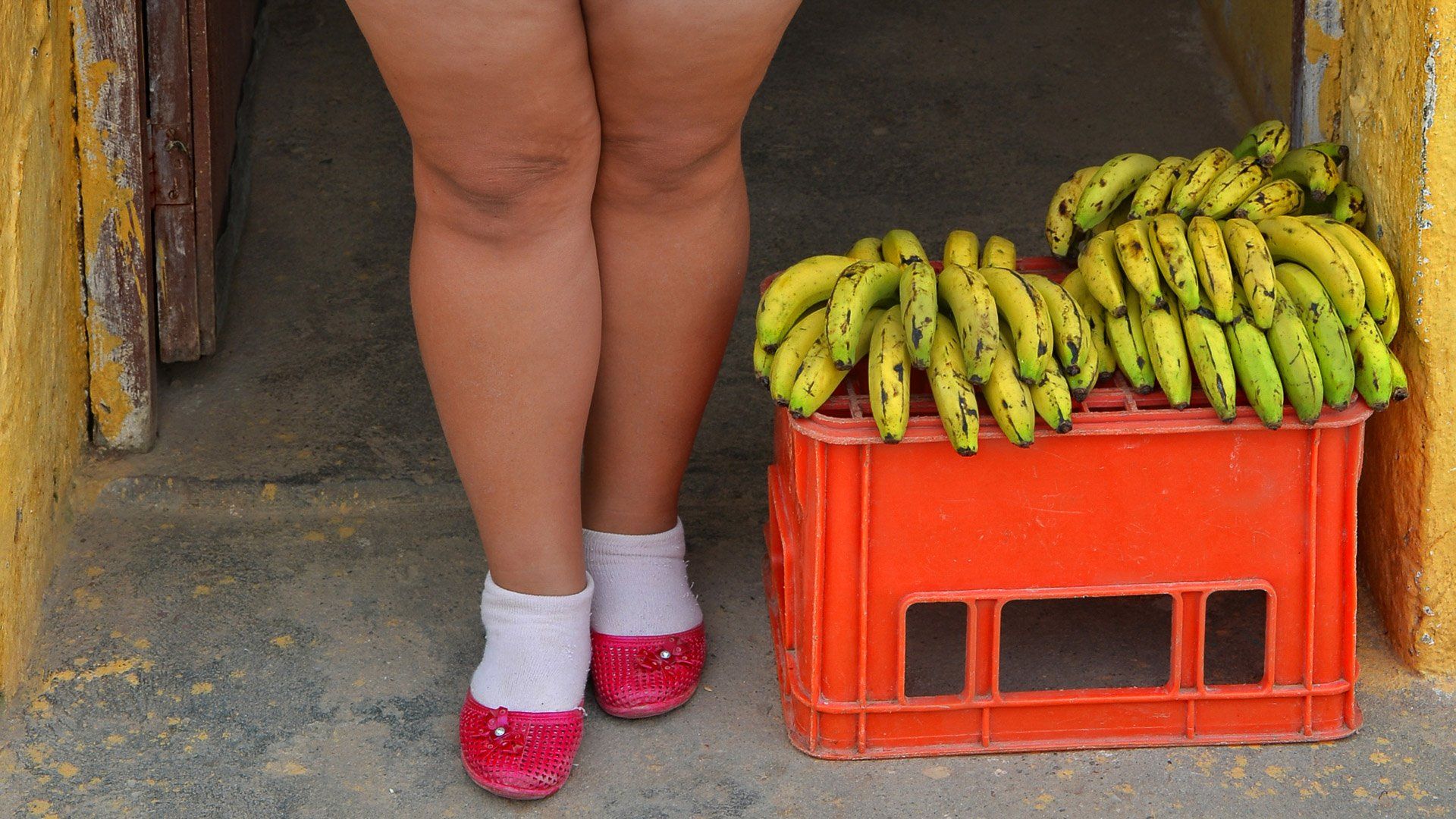 A woman is standing next to a crate of bananas.