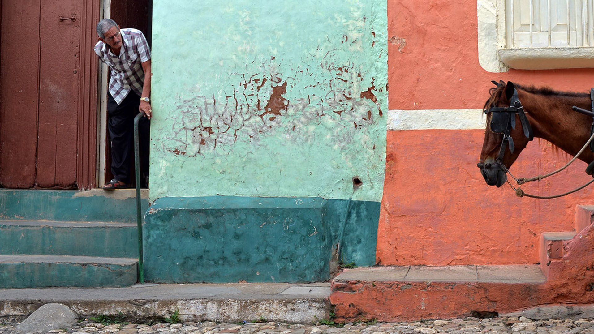 A man with a cane is standing in a doorway next to a horse drawn carriage.