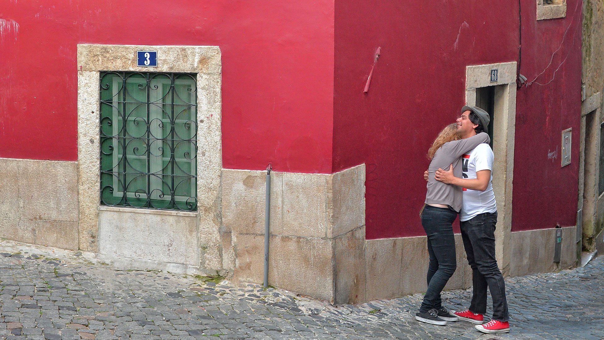 A man and woman hugging in front of a red building with the number 21 on it