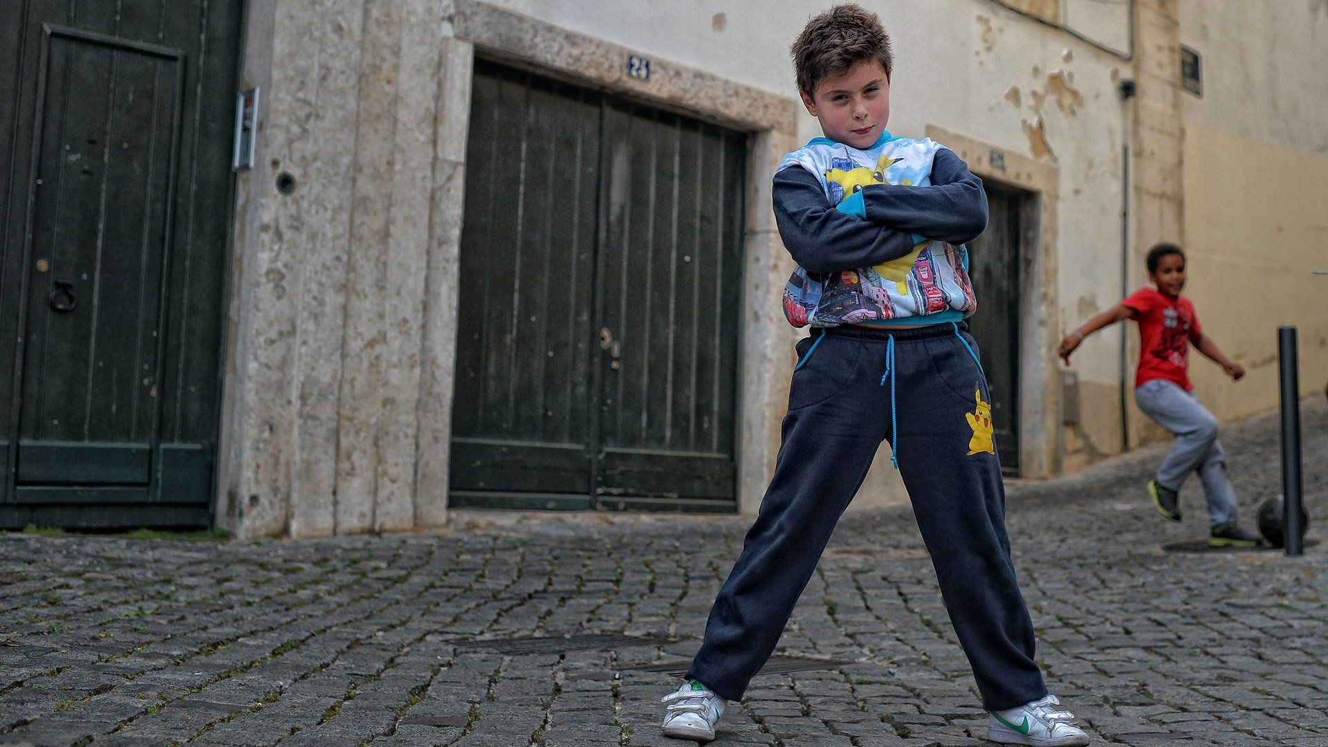A young boy is standing on a cobblestone street with his arms crossed.