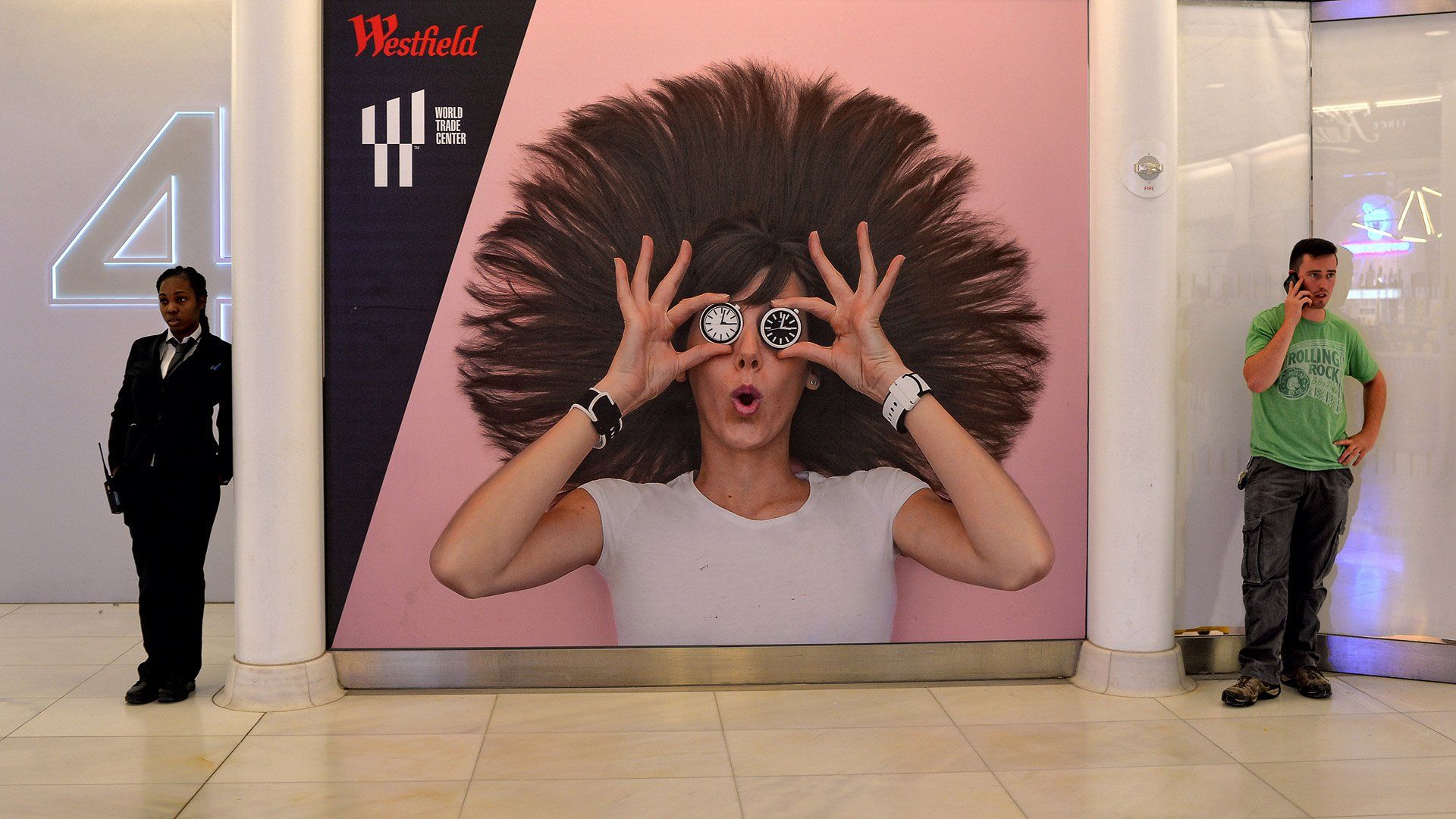 Two people are standing in front of a large poster of a woman with an afro