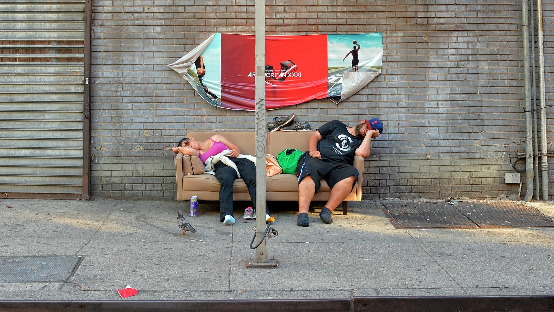A man and a woman are sleeping on a couch on the sidewalk