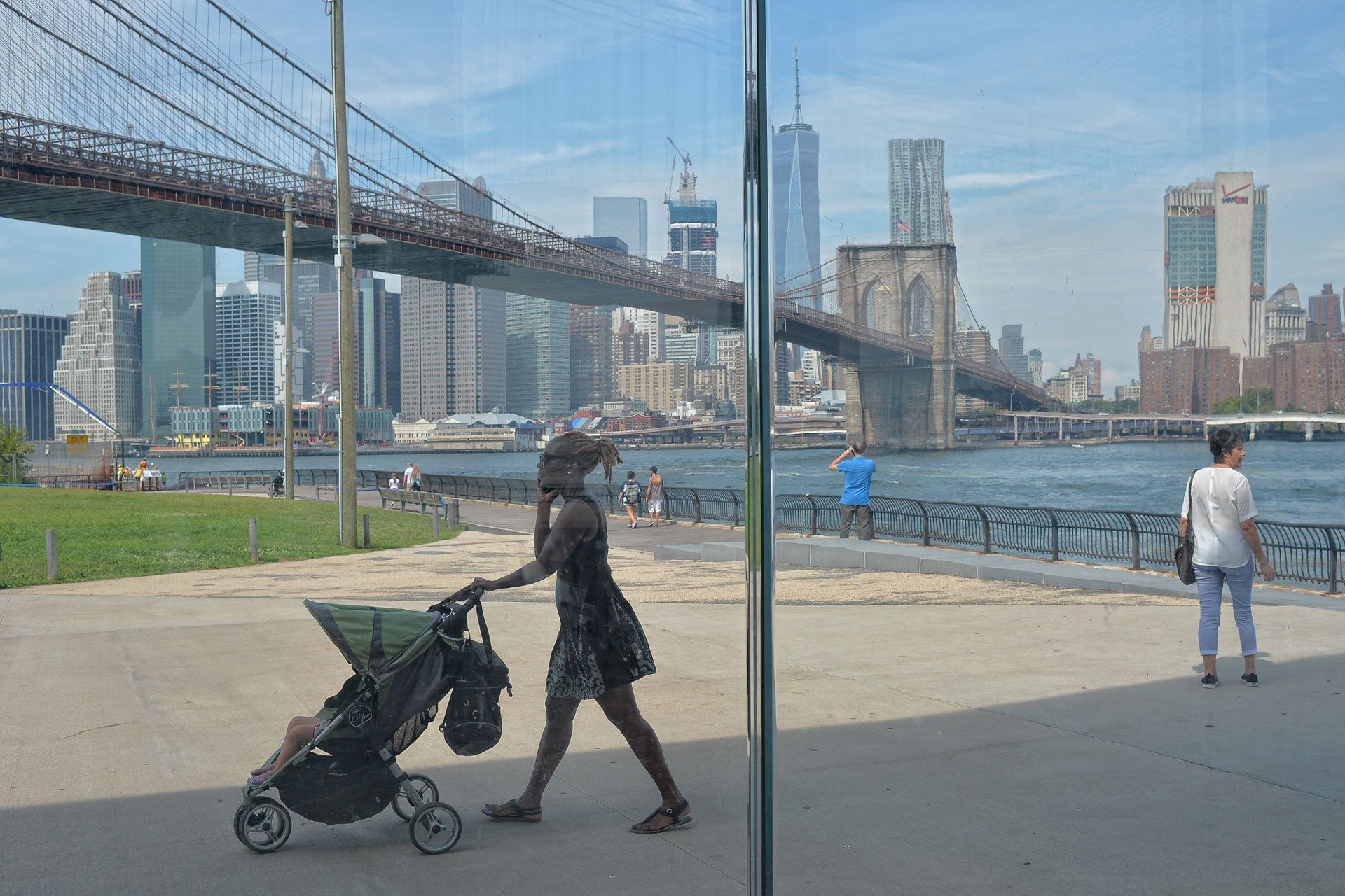 A woman is pushing a stroller in front of a bridge.