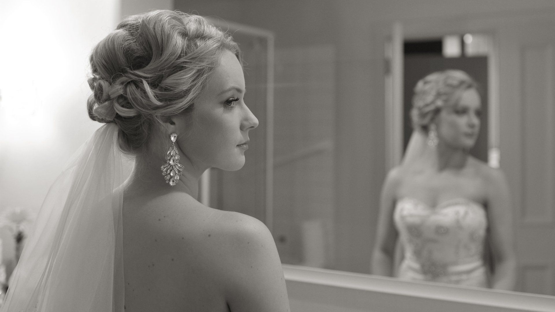 A bride in a wedding dress is looking at her reflection in a mirror.