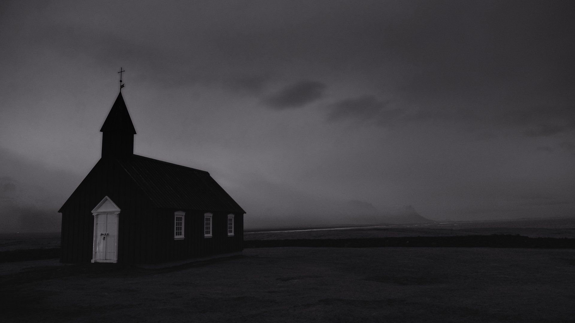 A black and white photo of a small church in the middle of a field.