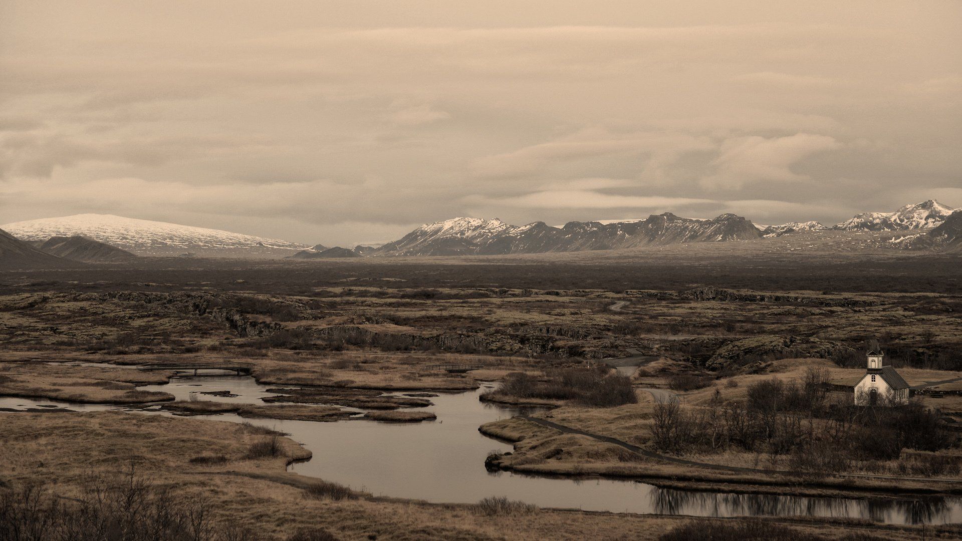 A black and white photo of a landscape with a river and mountains in the background.