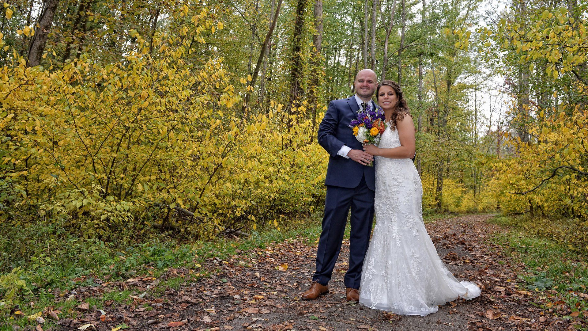A bride and groom are posing for a picture in the woods.