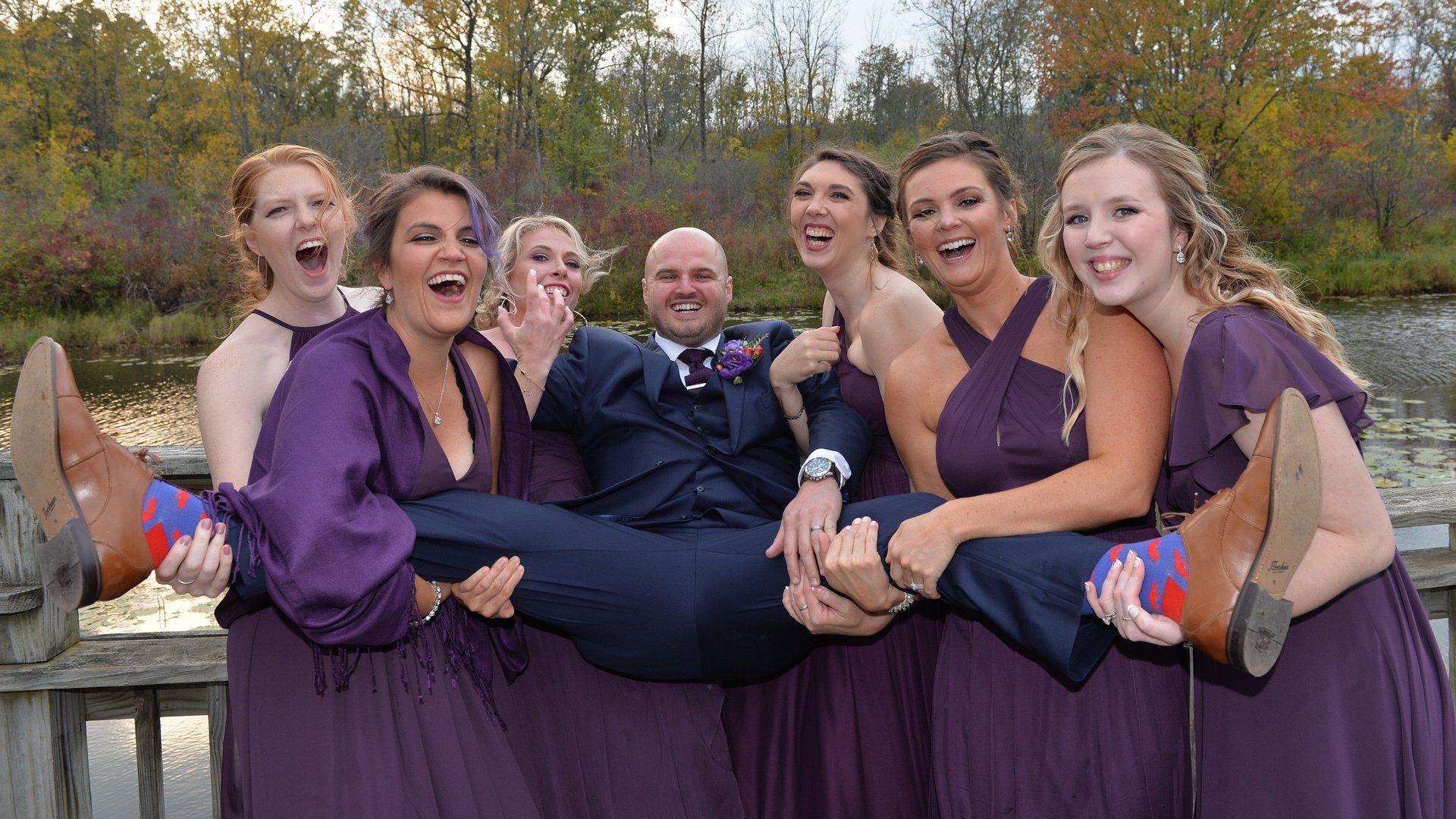 A group of bridesmaids are holding a groom in their arms.