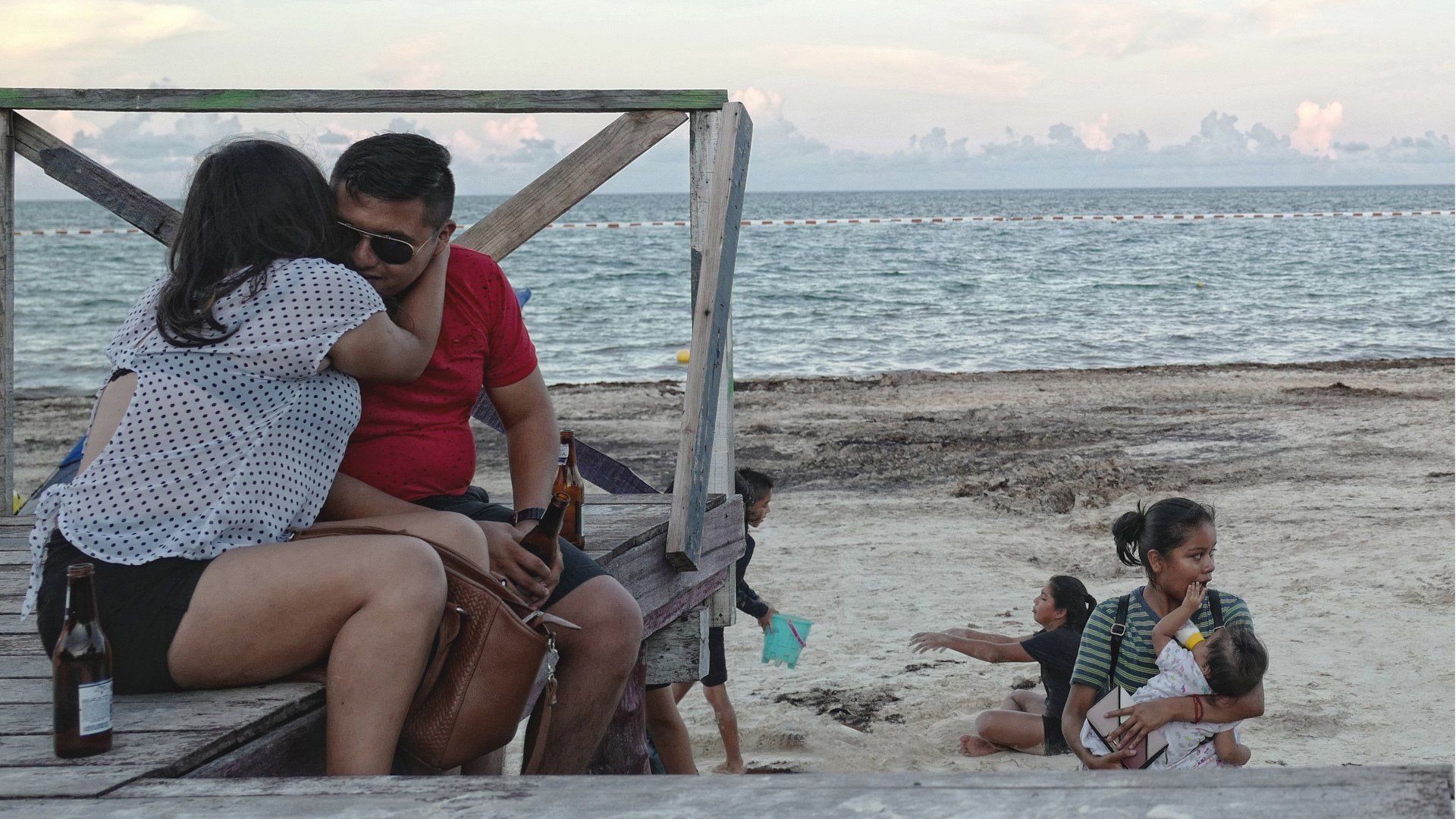 A man and a woman are sitting on a wooden bench on the beach.