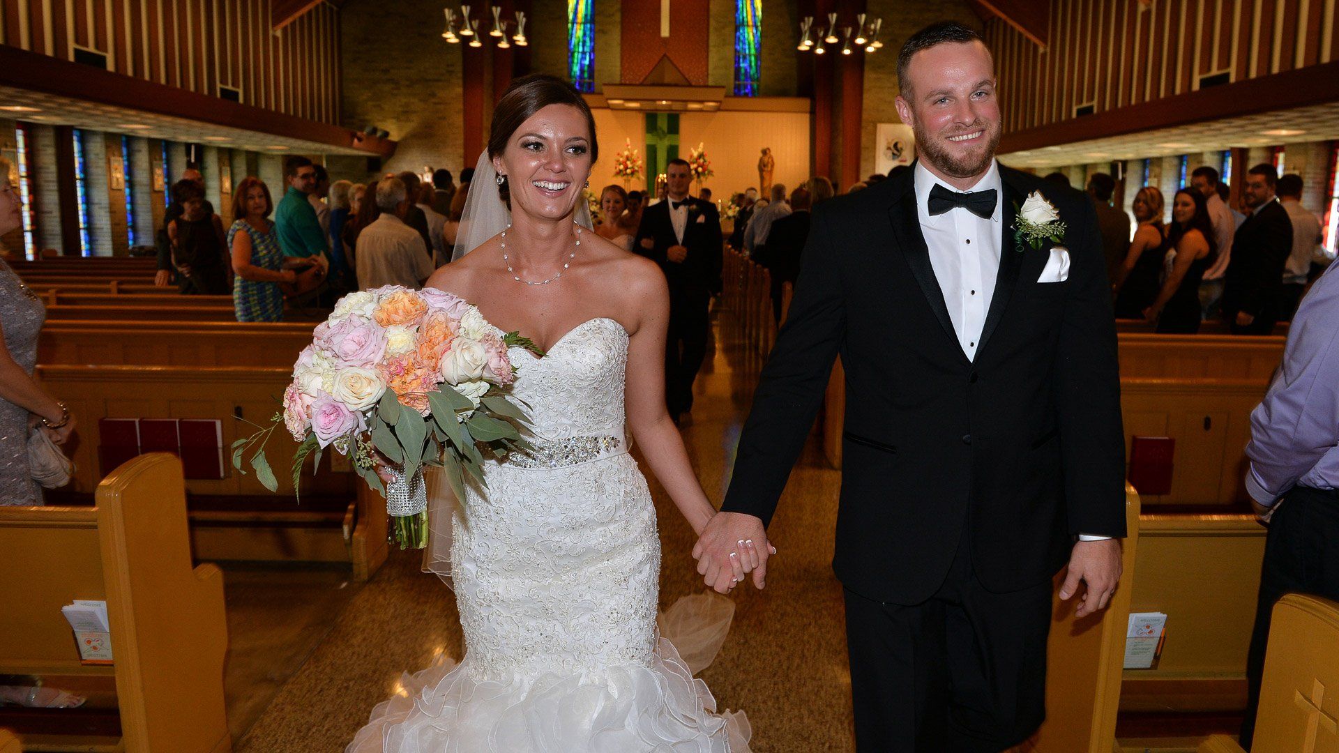 A bride and groom are walking down the aisle of a church holding hands.