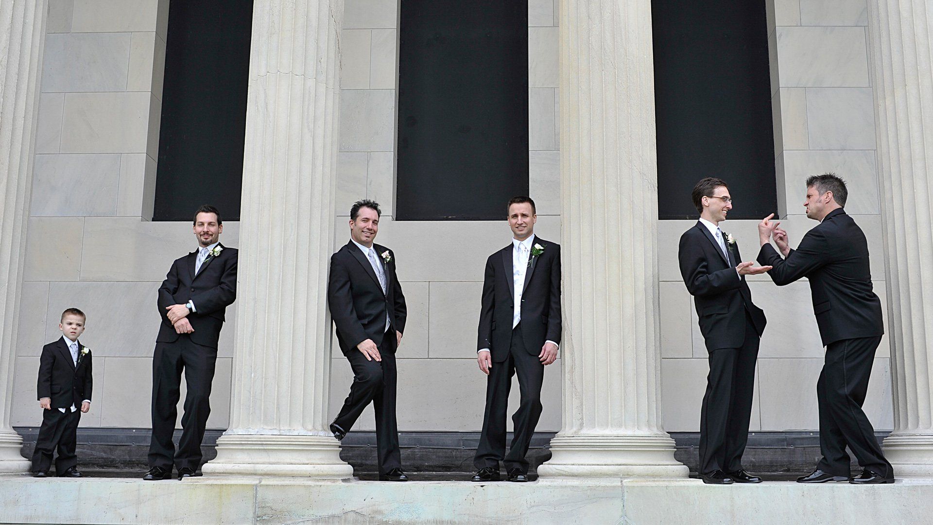 A group of men in suits are standing in front of columns.
