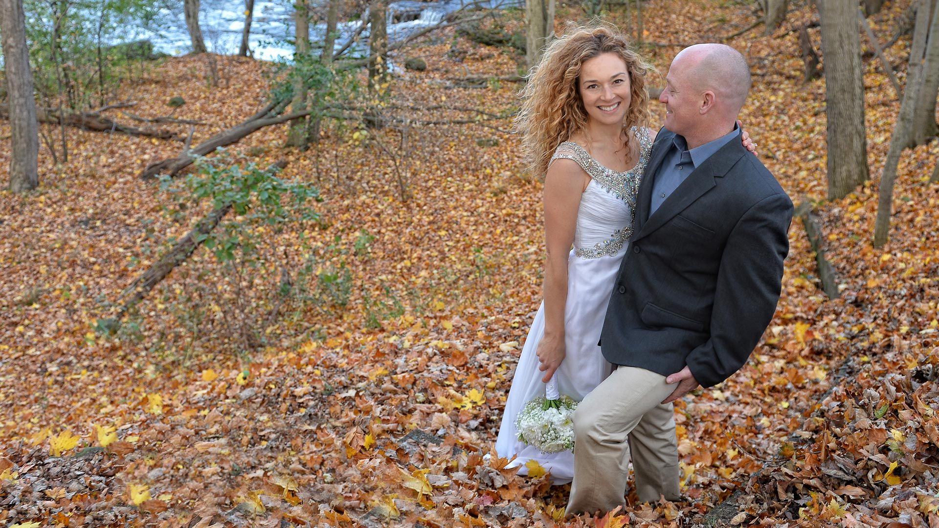 A bride and groom are posing for a picture in the woods.