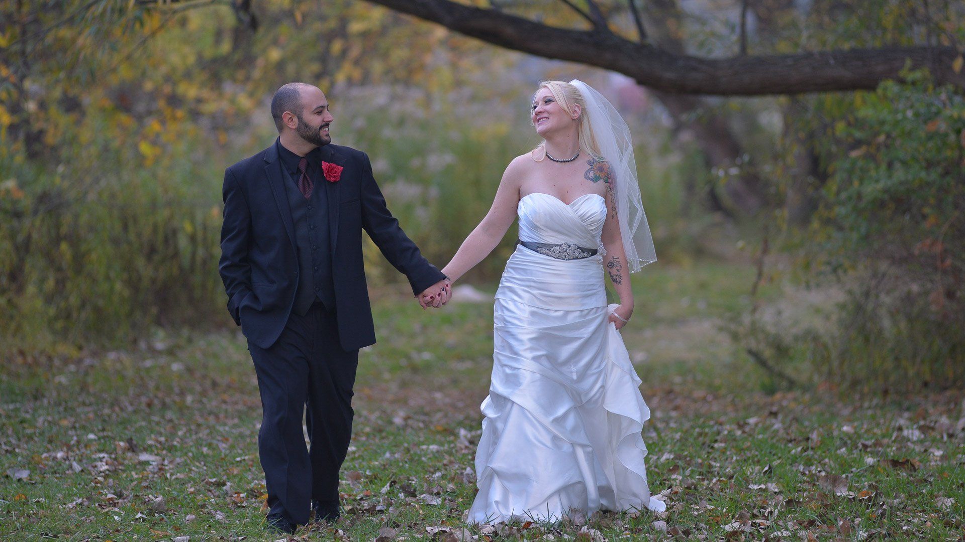 A bride and groom are holding hands while walking through a forest.