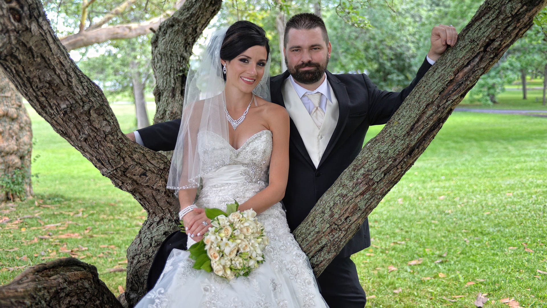 A bride and groom are posing for a picture under a tree.