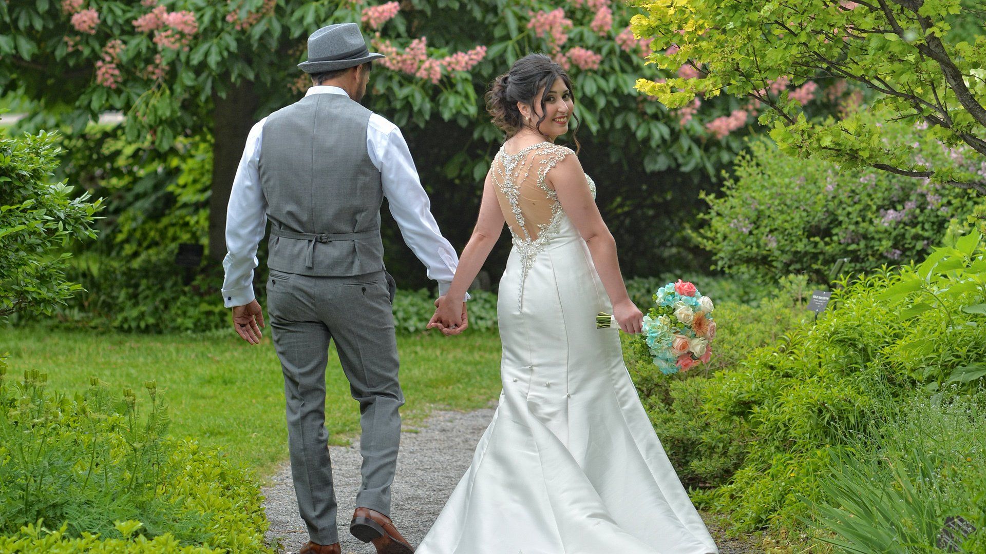 A bride and groom are holding hands while walking through a garden.