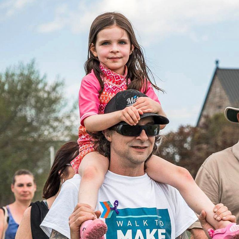 Une petite fille est sur les épaules de son père et marche le long du parcours de l'événement.