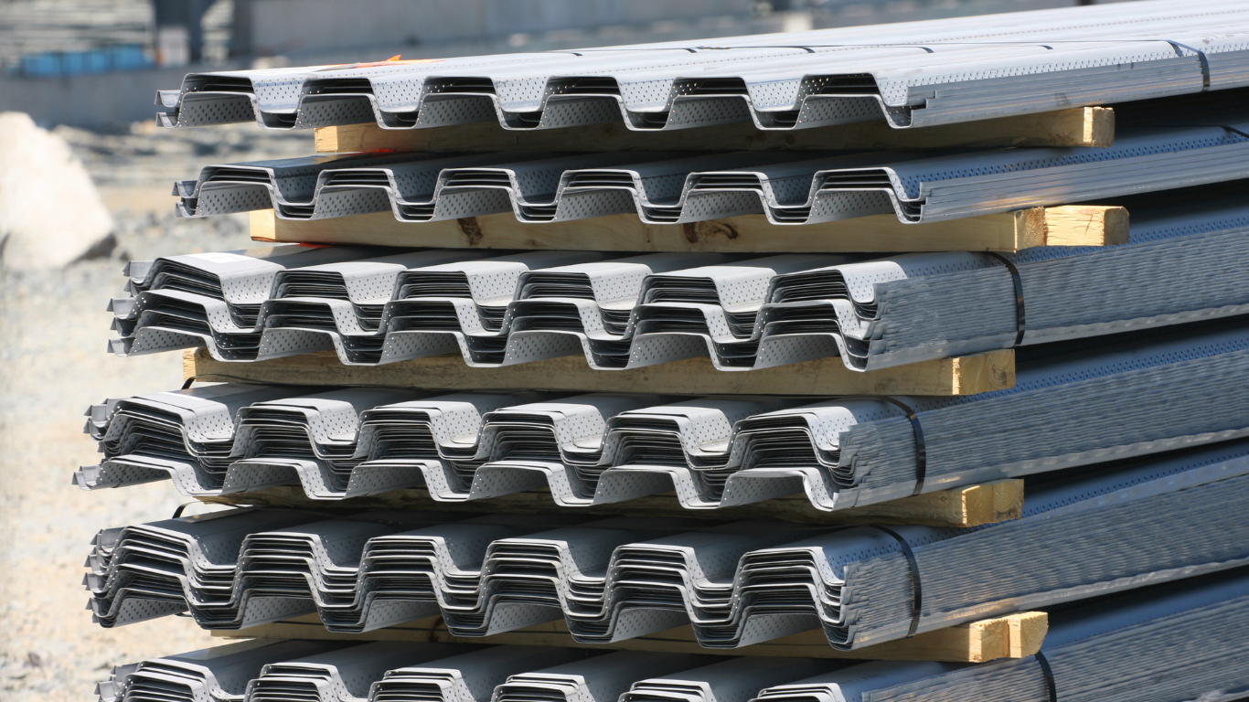 Sheets of corrugated metal roofing in brown and silver, stacked indoors.