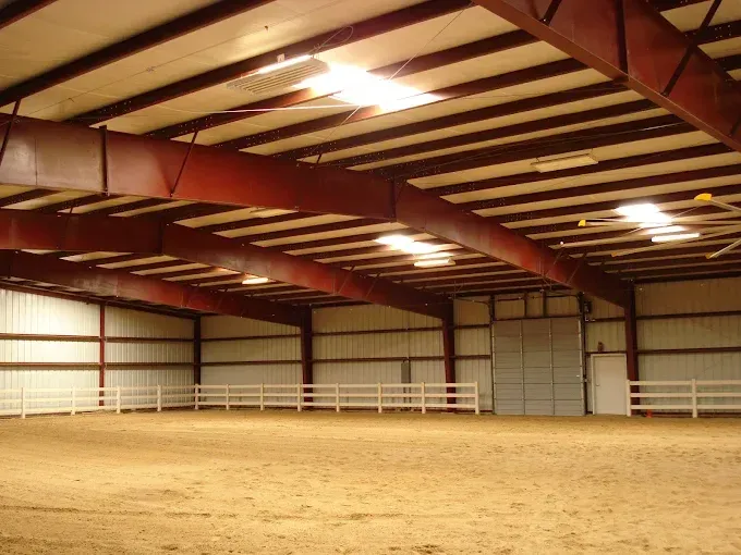 Large white metal building under a clear blue sky. A smaller wood structure is to the right.