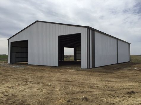 White metal agricultural building with large open bays on a dirt lot under a cloudy sky.