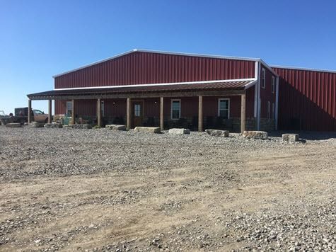 Red metal building with a porch, set on a gravel lot under a blue sky.