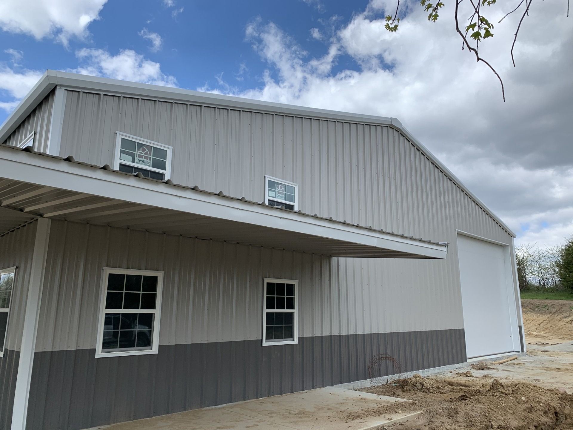 Gray and white metal barn with awning and windows under a cloudy sky.
