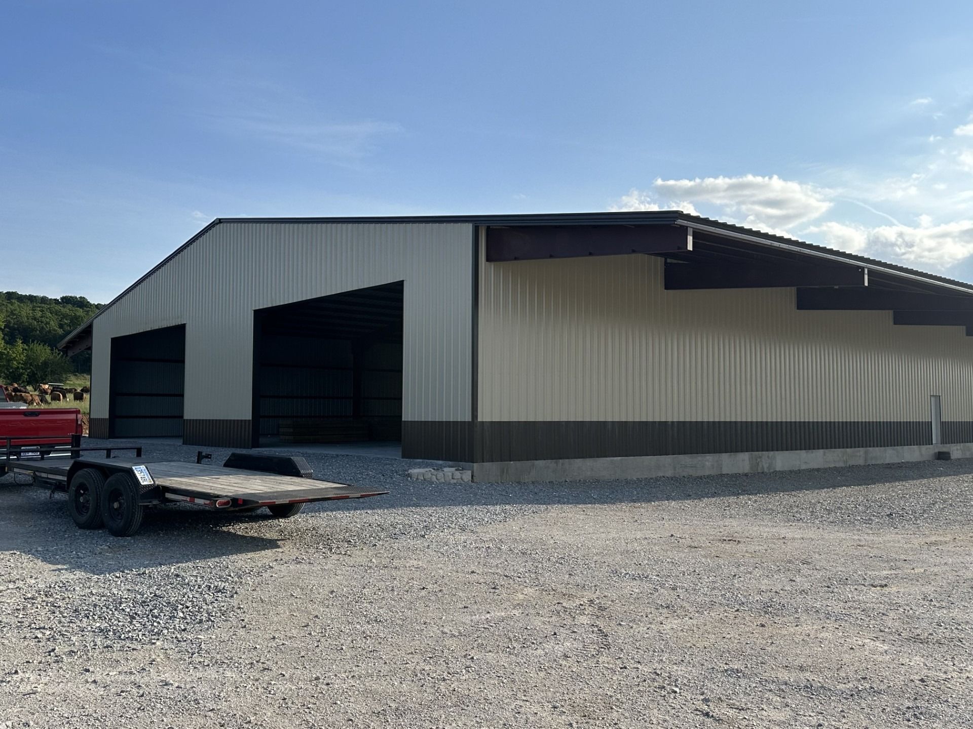 Tan and brown metal building with open bays, gravel lot, and a trailer.
