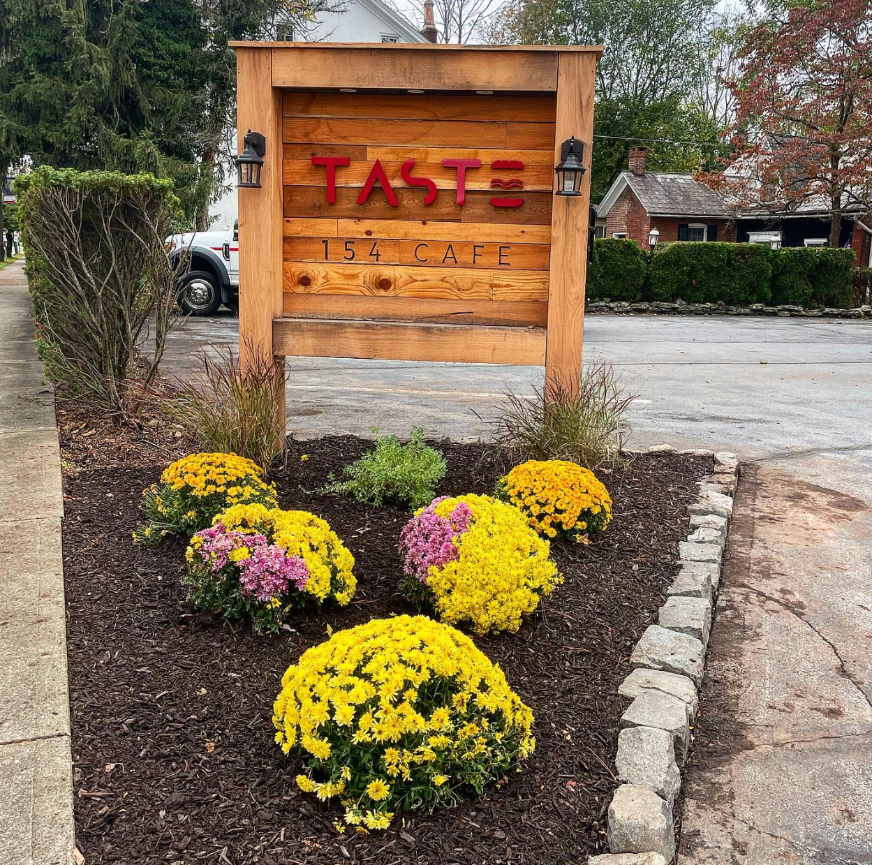 A sign for taste tea cafe is surrounded by flowers