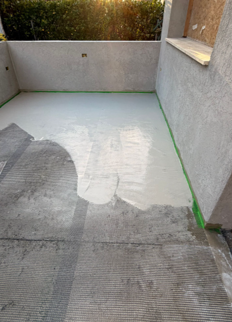 Cemento grigio chiaro appena gettato su un patio, con nastro adesivo verde lungo i bordi. Luce del sole dall'alto.