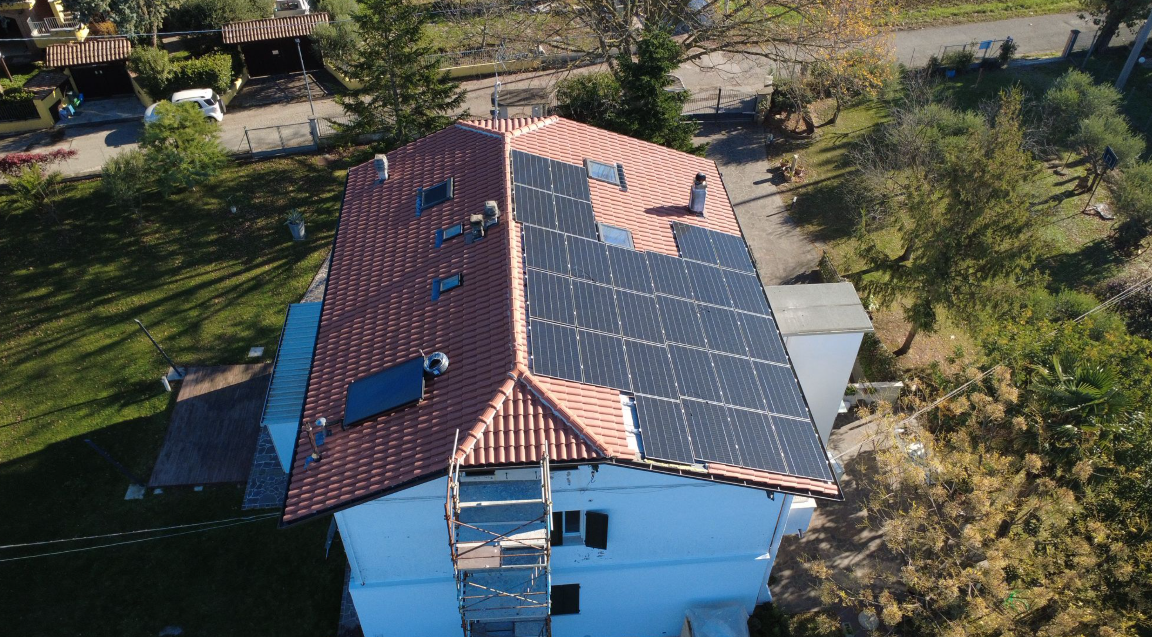 Casa con tetto di tegole rosse, pannelli solari e una scala sul lato, vista aerea.