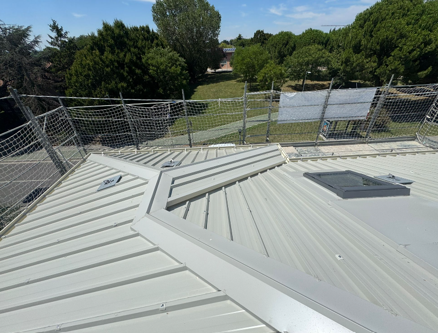 Tetto in metallo con ringhiere, incastonato in un paesaggio verdeggiante alberato sotto un cielo luminoso e soleggiato.