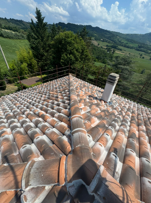 Tetto di tegole con camino, con vista sulle verdi colline e sul cielo azzurro.