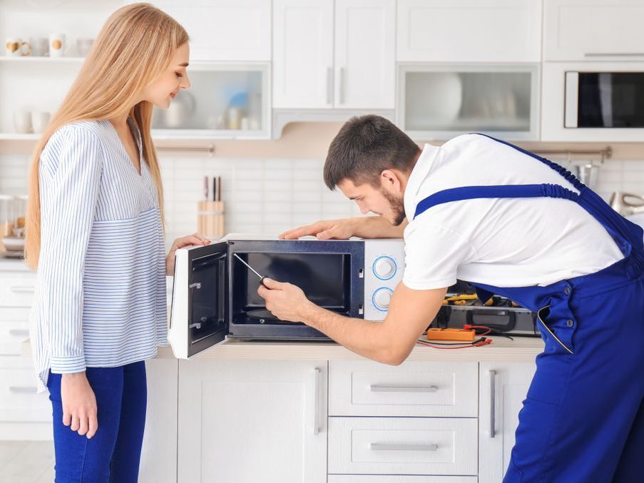 A woman watching the repairman fixing the microwave