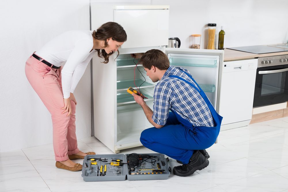 A woman watching the repairman diagnose her refrigerator
