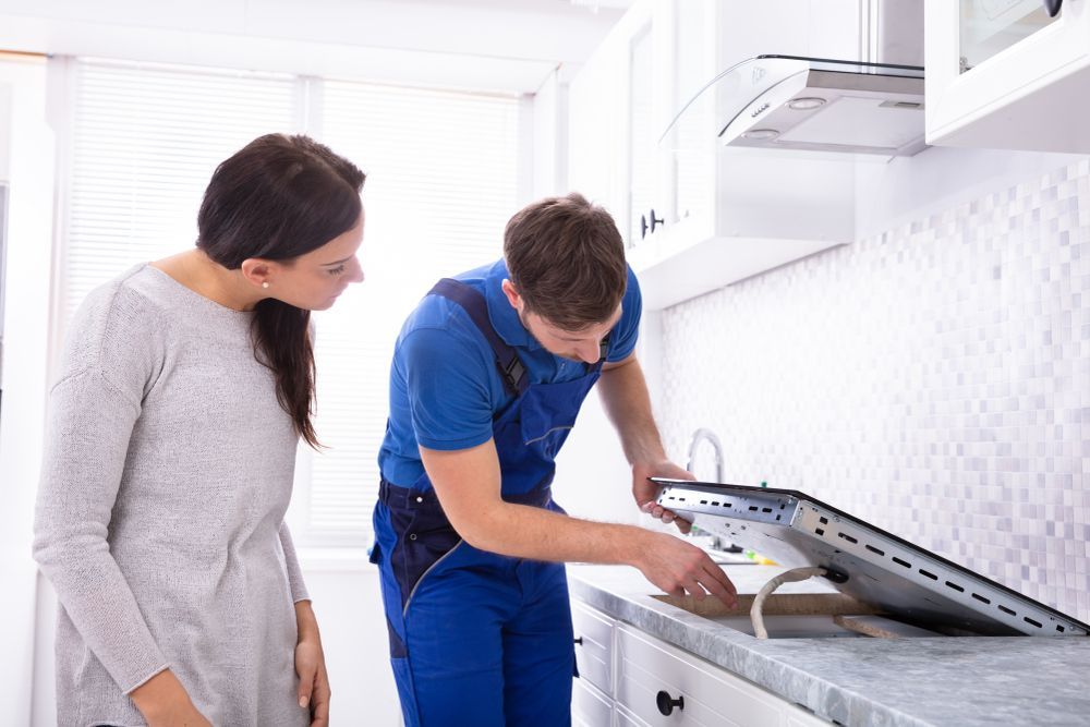 A woman watching the repairman fixing the stove